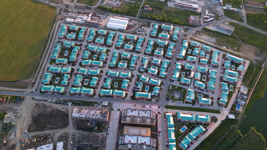 Aerial high angle footage of a brand new residential neighbourhood seen from above. Drone shot of suburban houses with blue roof and streets on a summer afternoon. Top down view of buildings
