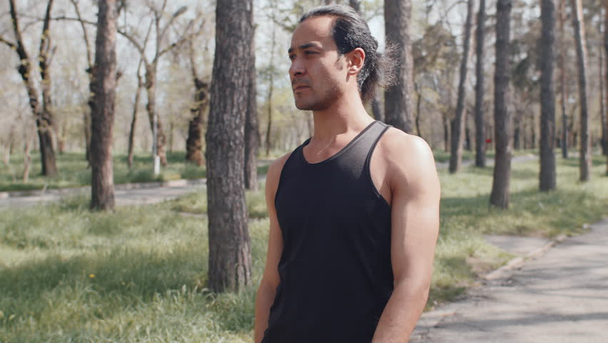 Sportsman engaging in arm stretches while warming up in a lush green park