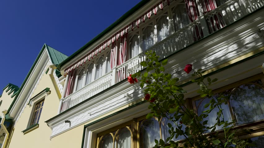 A detailed shot of a Victorian-style villa's upper balcony, featuring a red and white striped awning with decorative red tassels. The architectural details of the pointed arches and intricate