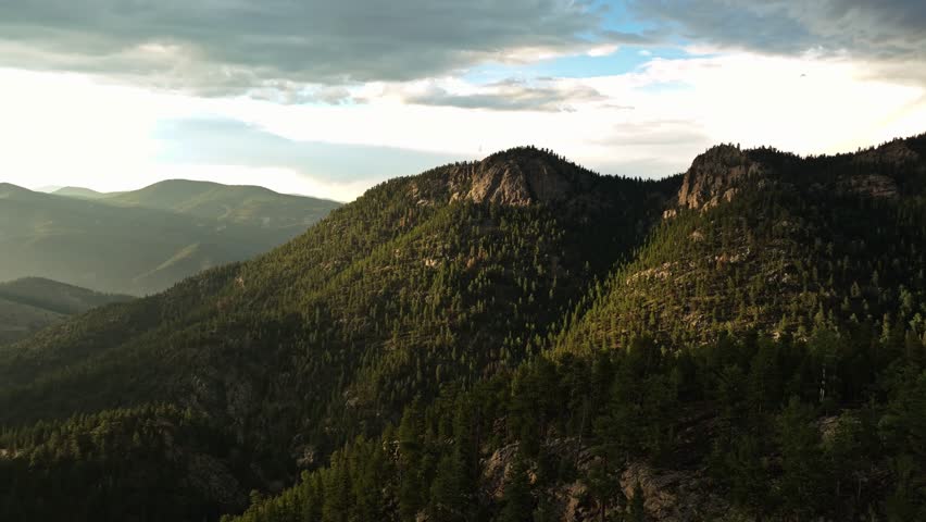 Aerial trucking pan view of Idaho Springs, Colorado, showing the forested mountain ranges and soft evening light