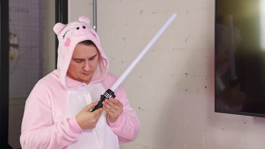 Portrait of man in pink kigurumi pajamas with plastic sword stands at screen, presentation of creative advertising company, speech to children fans of the game, edutainment Dream teamwork, imagination