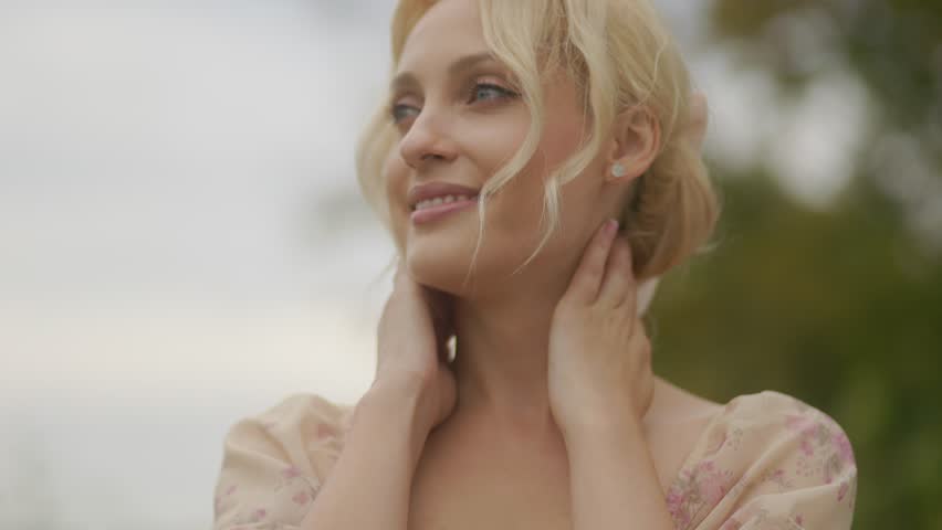 A joyful middle-aged blonde woman smiling, with sunlight illuminating her face in a peaceful outdoor setting.