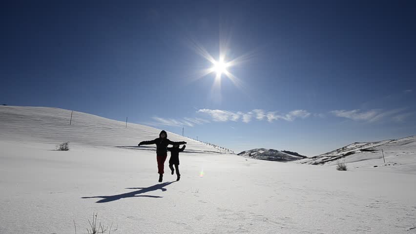 Two kids boy and girl enjoying play run on snow slope. Girl runs toward camera,