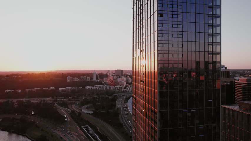 A tall, glass skyscraper captures the sunset