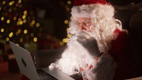Santa Claus reading letters by laptop, touching eyeglasses and looking at screen . Amazed emotional wizard with portable computer sitting alone in decorated living room in his home, portrait shot - Powered by Shutterstock - Get 15% off with code: PIKWIZARD15