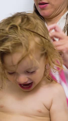 Mother affectionately holding her little son and drying him with a towel in the bathroom after showering him.