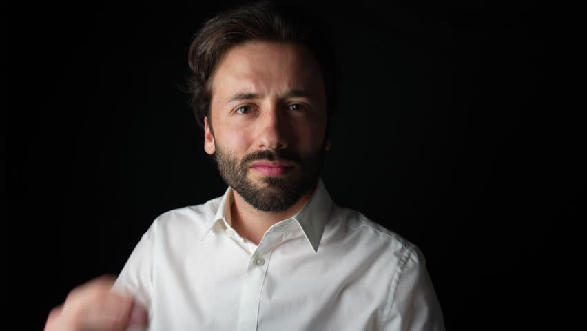 A young Caucasian man in a white shirt smiles at the camera while casually adjusting his hair