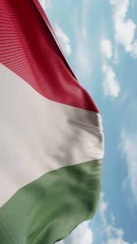 Wavy flag of Hungary blowing in the wind in slow motion. Waving colorful Hungarian flag team symbol abstract vertical background. Blue sky with clouds. World countries flying flags concept