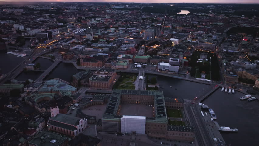 Aerial views showcase Stockholm city center illuminating during blue hour, highlighting the Royal Palace and canals with boats