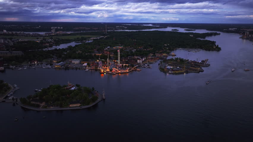 Stockholm city skyline illuminating during sunset with boats sailing. Grona Lund amusement park tower lights reflect on the water