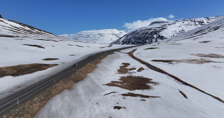 Aerial view of snow-covered mountains and an open road under a blue sky, southeast of Akureyri, Iceland.