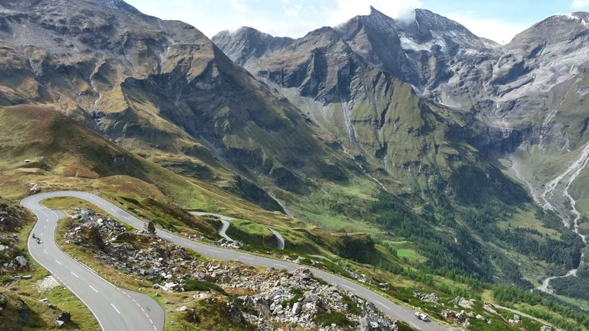 Motorcycles and cars cruising a scenic asphalt road in the tranquil Austria mountains . Majestic rocky Alps .