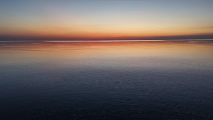 Drone shot skimming the surface of a calm lake at sunset