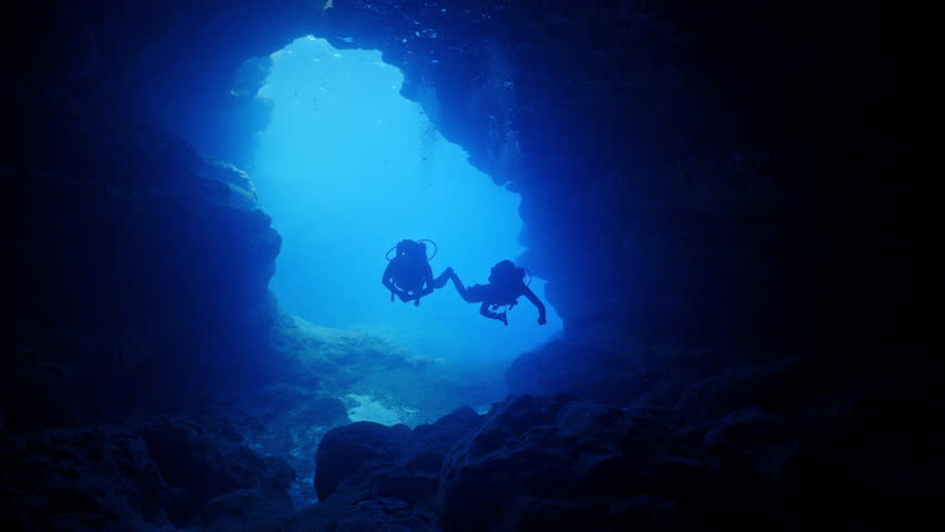 SCUBA Divers swim into an  underwater cave from a blue entrance