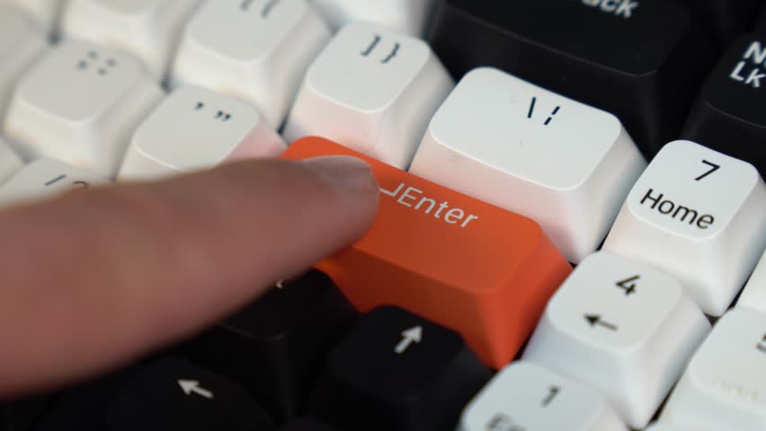 Finger pressing an enter key. Computer user hitting the enter key, up close. Close-up of a finger pressing the red enter button on a custom keyboard.