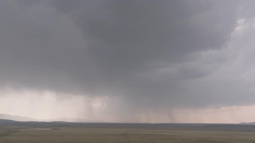 Rain showers in the distance sweep over a vast flatland under heavy gray clouds