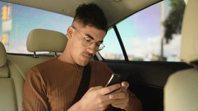 Man with Glasses Using Cell Phone in Back Seat of Car. Focused Male Passenger in Brown Shirt Engaging with Smartphone While Traveling, Emphasizing Urban Mobility and Digital Connectivity - Powered by Shutterstock - Get 15% off with code: PIKWIZARD15
