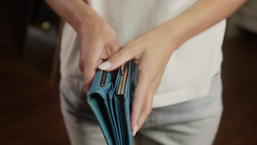 Woman shows an empty blue wallet, revealing a lack of money inside. The scene highlights financial struggles and the challenges of managing personal finances