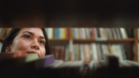 Smiling woman picking a book from the shelf and reading a few pages in a quiet bookstore. Happy young reader enjoying her time in a cozy library while browsing through the shelves. - Powered by Shutterstock - Get 15% off with code: PIKWIZARD15