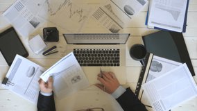 Top view hands of young businessman looking at diagrams with statistic on paper and typing text on laptop keyboard at white desk. Male arms of manager working on computer at wooden table in office - Powered by Shutterstock - Get 15% off with code: PIKWIZARD15