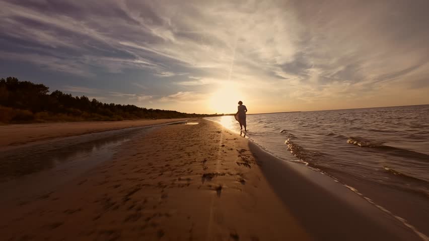  woman run along the beach during sunset, with a serene ocean and dramatic sky in the background. The warm, golden light adds to the tranquil atmosphere.