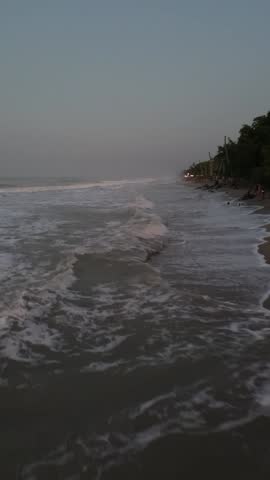 A stunning drone captures the vibrant sunset over Palomino beach in Colombia, flying above swaying palm trees and waves, with a few people strolling along the peaceful shoreline