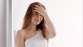 A woman with flowing hair stands in a bright room, gazing thoughtfully at her reflection in the mirror. The sunlight accentuates her serene expression and elegant pose. - Powered by Shutterstock - Get 15% off with code: PIKWIZARD15