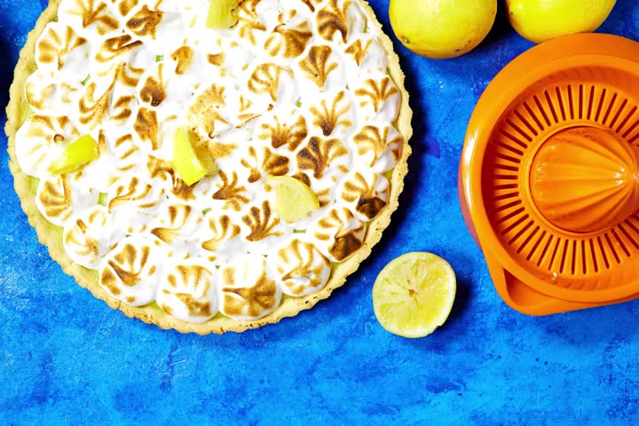 Traditional french lemon Meringue tart with fruits and orange juicer on blue grunge background
