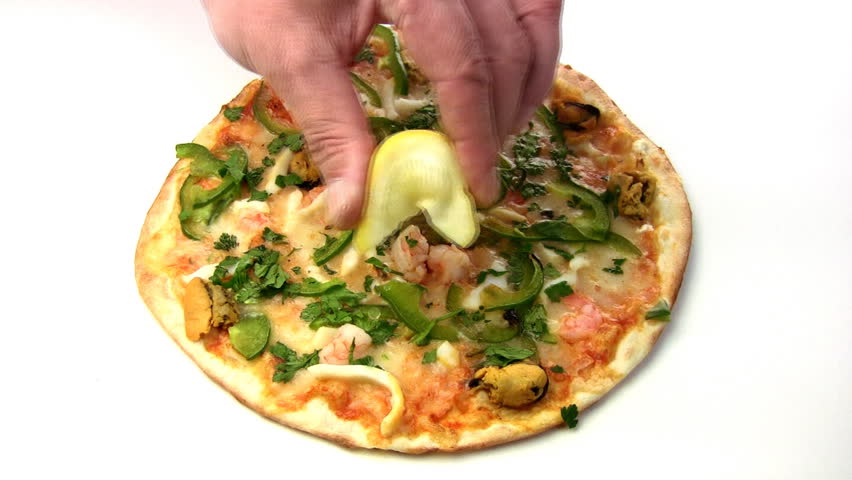 Men's hand to squeeze the lemon on the pizza with seafood (shrimp, mussels), and