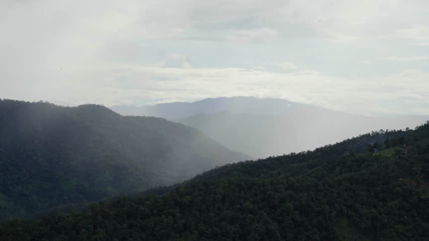 4K HD cinematic view of a cloudy and foggy darkening mountain landscape in Mae Tang, Thailand. rain approaching from background, dramatic, atmospheric landscape enveloped in mist and rain, smoke fire