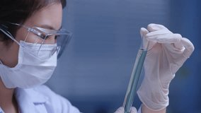Laboratory background footage from close up side view. The female scientist holding a test tube contains blue liquid in hand and carefully observing. Copy space for text - Powered by Shutterstock - Get 15% off with code: PIKWIZARD15