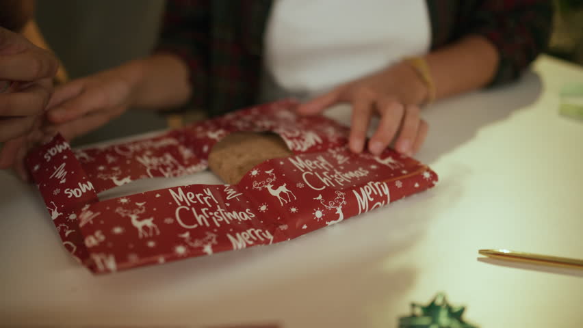 Close up of gift wrapping process, showcasing teamwork in crafting festive christmas present using decorative paper and tape