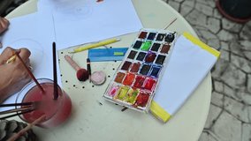 Creative back to school art activity with watercolor painting on paper, showing hands sketching and coloring on a white table outdoors - Powered by Shutterstock - Get 15% off with code: PIKWIZARD15