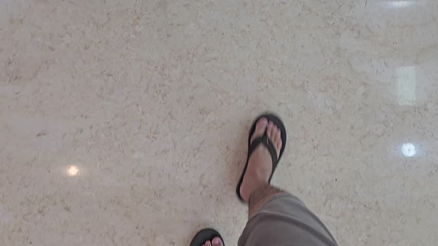 man walking on the floor wearing black sandals, wearing shorts, top view only legs.