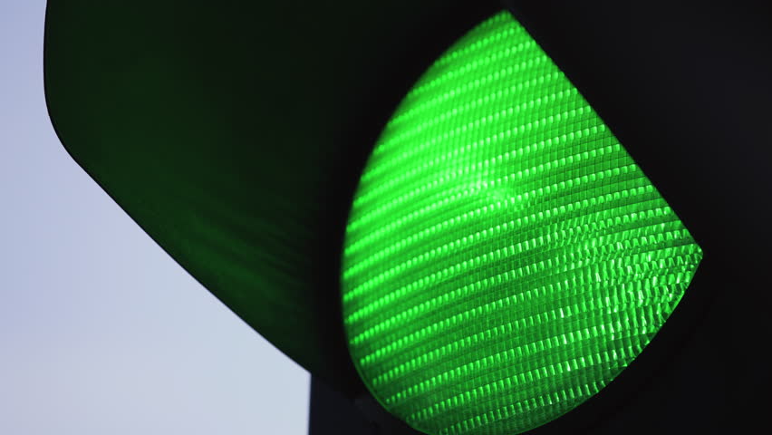 Extreme close-up view of vertical traffic light in city turns green, city crossroad, car traffic control, cloudy day