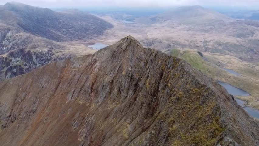 Drone captures the majestic sharp Crib Goch Mountain from aerial perspective, revealing its rugged ridges and dramatic peaks against vast open landscape at Snowdonia National Park, Wales