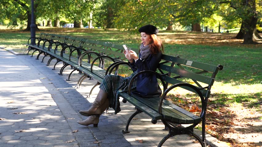 Young Asian woman tourist relaxing during autumn foliage season sitting on a lawn chair in Central Park, New York, USA.