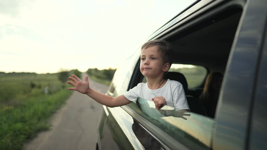 Boy enjoys road trip with family. Young boy leans out car window on scenic road. child feels wind during family car journey. Boy embraces freedom during road trip. Family road trip with boy in car.