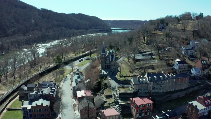 Aerial establishing orbit of a town surrounded by mountains, with homes and buildings nestled in the valley under a bright sky, Harpers Ferry West Virginia in sticks season