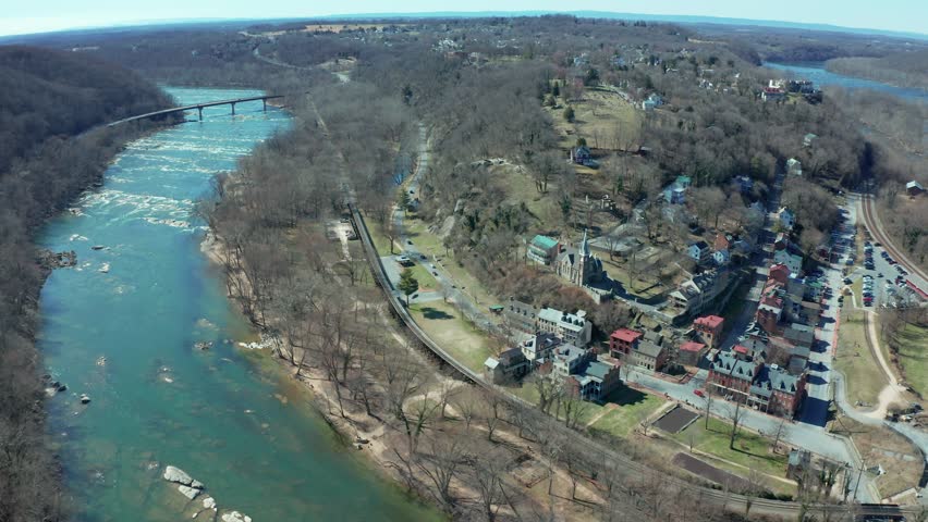 Aerial view of a small old historic downtown surrounded by river and mountains, with scattered buildings, roads, and train tracks