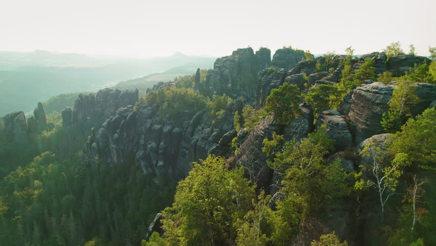 Aerial view of towering rock formations surrounded by dense green forest in Schrammsteine Elbe Sandstone Mountains Germany