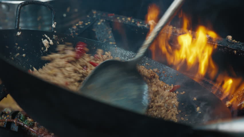Anonymous person stirring minced beef with red pepper slices bubbling in oil in overheated wok pan over flame. Ground beef being browned in skillet with chopped vegetables during cooking process.