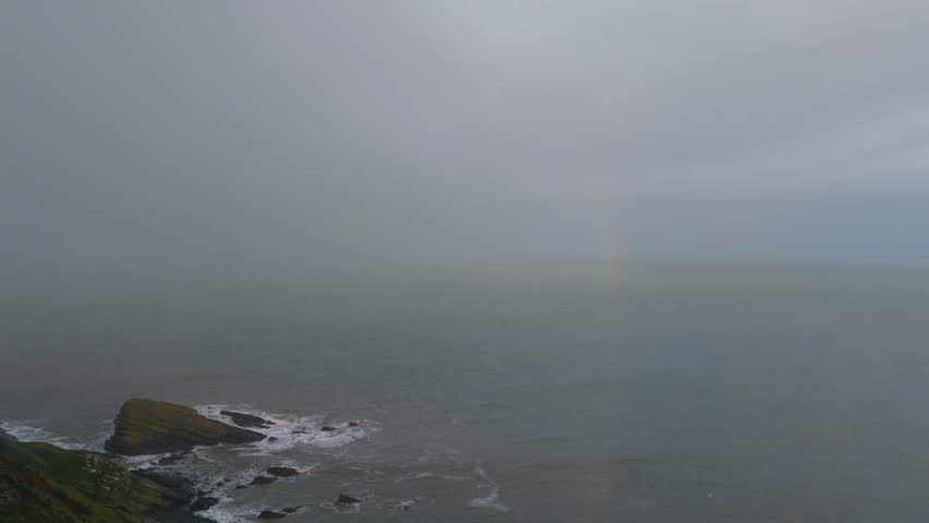 A powerful thunderstorm pounds the New Quay coastline as a rainbow forms in the bay
