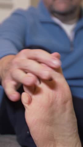 Vertical view of a man checking his toes due to foot pain. Living room set. Shallow depth of field.  	