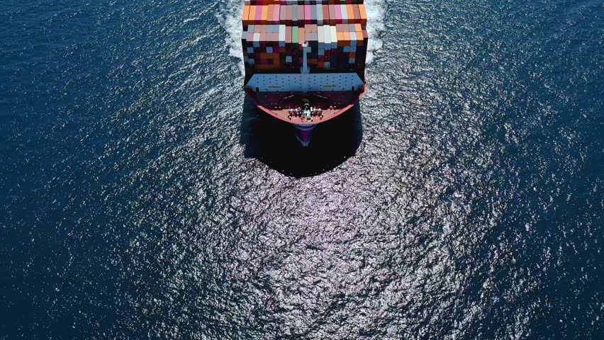 Aerial front view of a very large industrial container cargo carrier ship passing by with speed