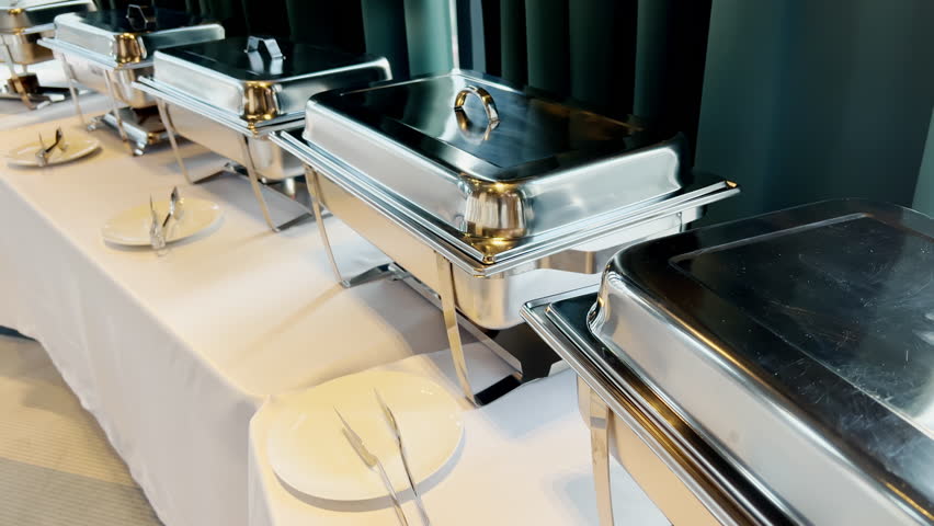 Stainless Steel Buffet Dishes with Plates and Tongs Lined Up in Hotel Catering Setup. Concept of Chafing Dish, Food Warmer, Banquet, Hotel Dining, Serving Equipment, Hospitality, Food Service