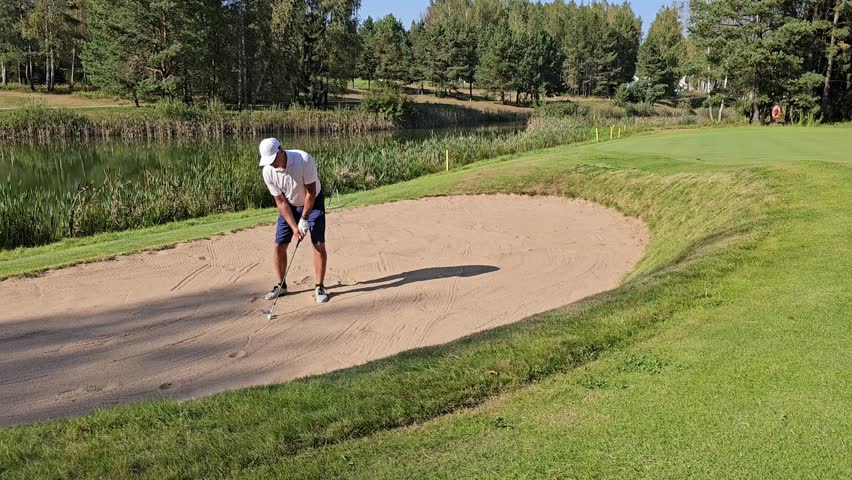 Golfer practices short game techniques in a sand trap at a lush green golf course