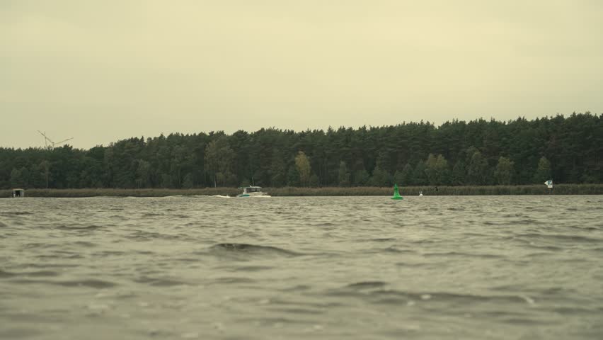 boat drives over river and hydro foil surfer try to catch the waves with forrest on coastline in slow motion