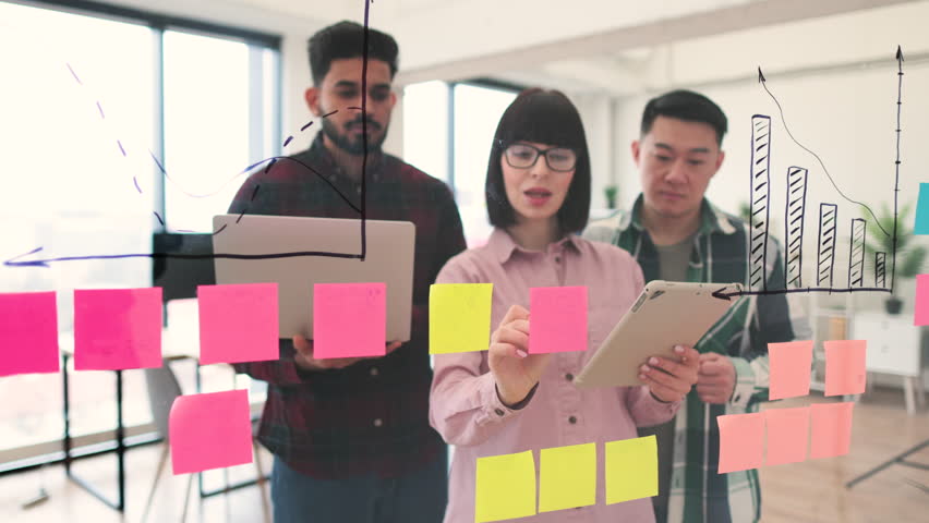 Team of young professionals brainstorming and collaborating using sticky notes on glass wall in modern office. Discussion focused on project planning, organization, and innovation. - Powered by Shutterstock - Get 15% off with code: PIKWIZARD15
