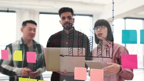 Group of professionals working together in open office environment with charts and sticky notes on glass board illustrating business strategy and ideas - Powered by Shutterstock - Get 15% off with code: PIKWIZARD15